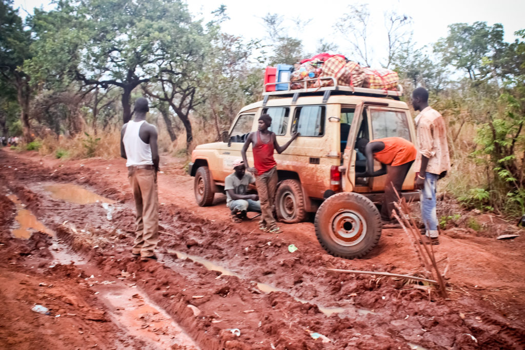 South Sudanese men change flat tire on muddy road in South Sudan